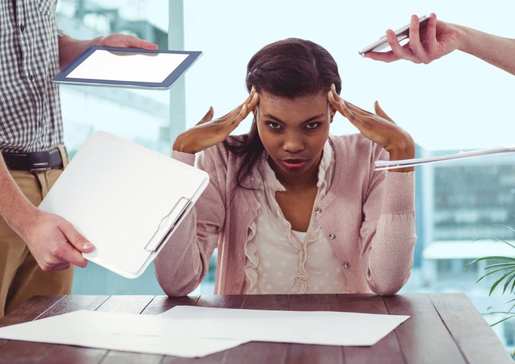 Why CRM and ERP Systems Are Strategic for Business Efficiency - INFINION Technologies Frustrated woman at a desk during a tense office meeting as teammates hand over a tablet and clipboard with papers on the table.