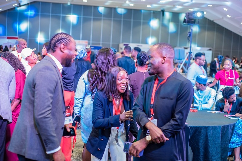 TEDxMaitama 2026 Digital Transformation in Abuja Nigeria - INFINION Technologies Professionals networking at a conference, smiling and chatting near a round table with event badges visible in the background.