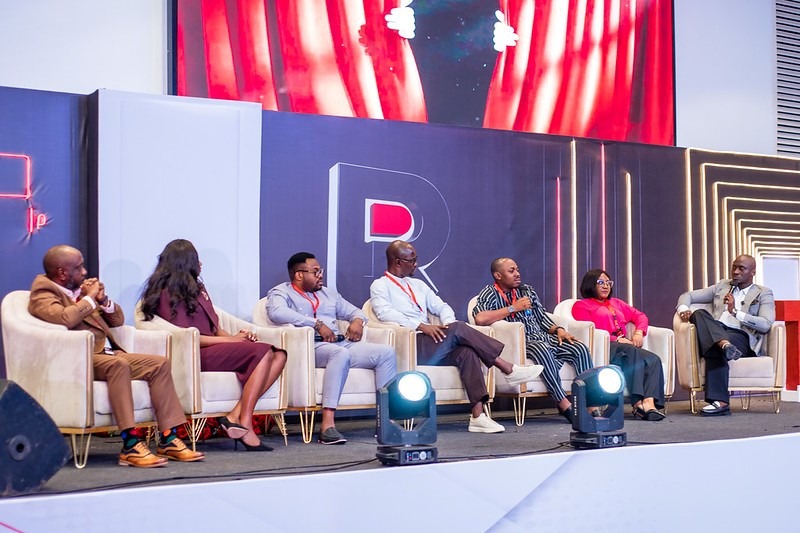 tedx roundtable INFINION - INFINION Technologies Panelists seated in chairs on a stage during a conference panel discussion, microphones visible and a large backdrop behind them.